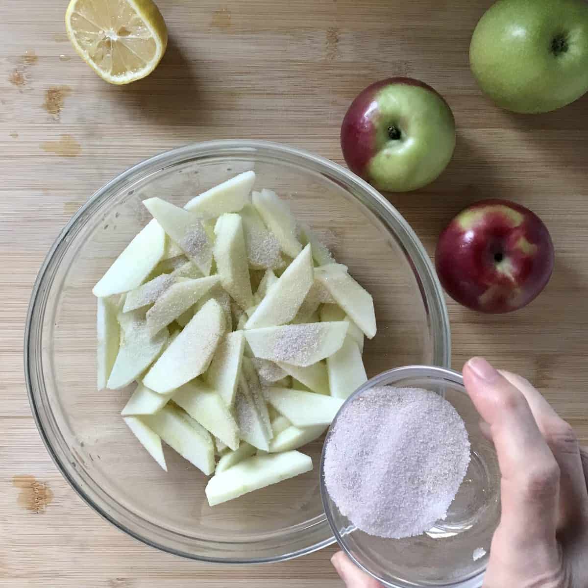 Cinnamomn sugar being sprinkled over sliced apples. 