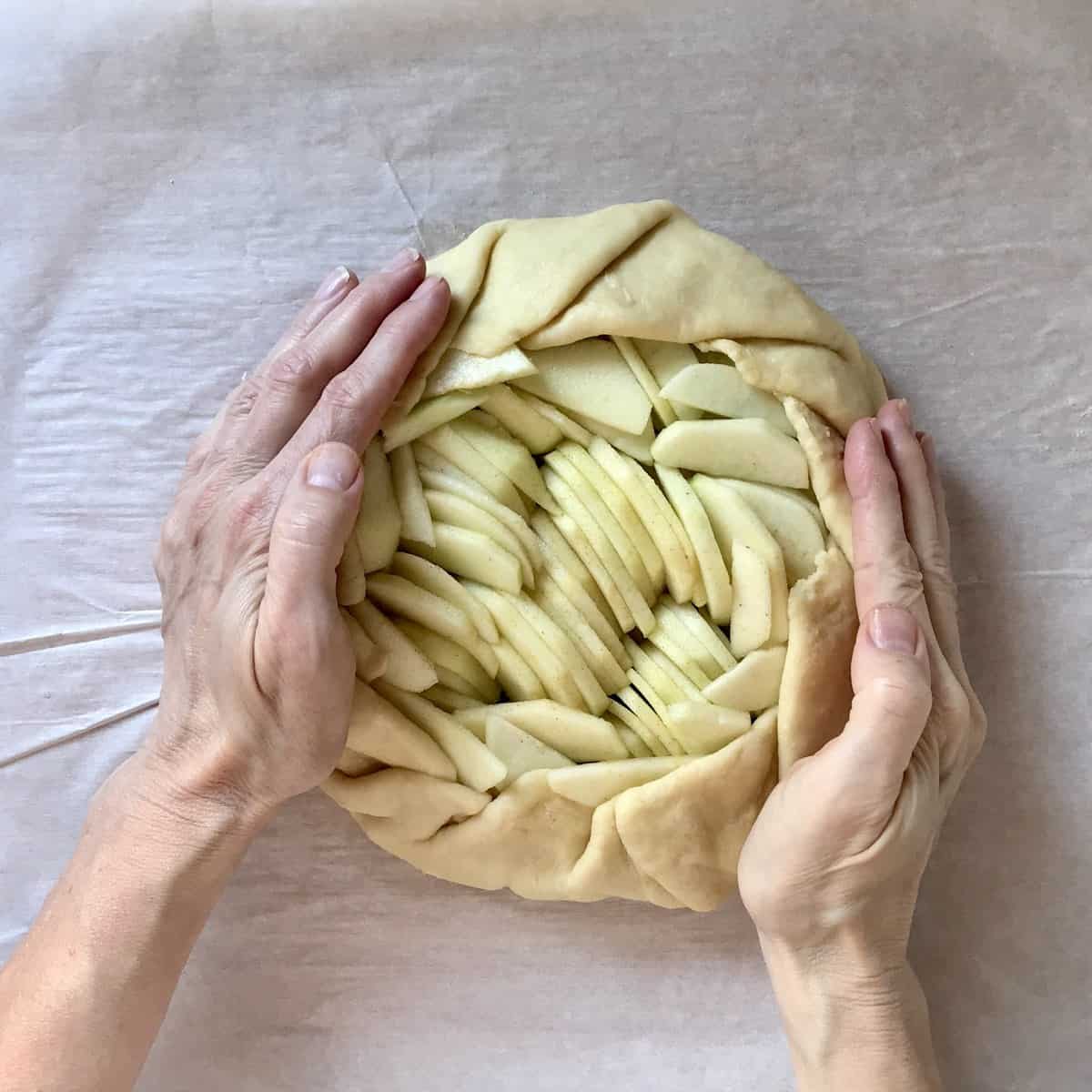 The crust of an apple crostata being compressed with sliced apples.