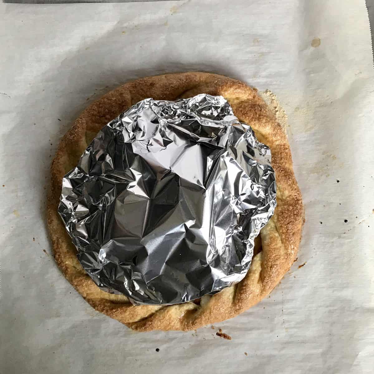 Aluminum foil covering part of an open faced apple pie. 