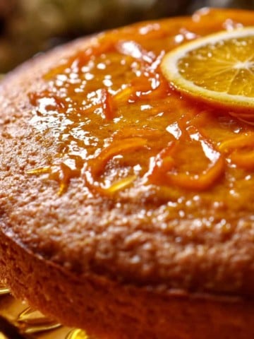 A glazed orange juice cake garnished with one slice of orange.