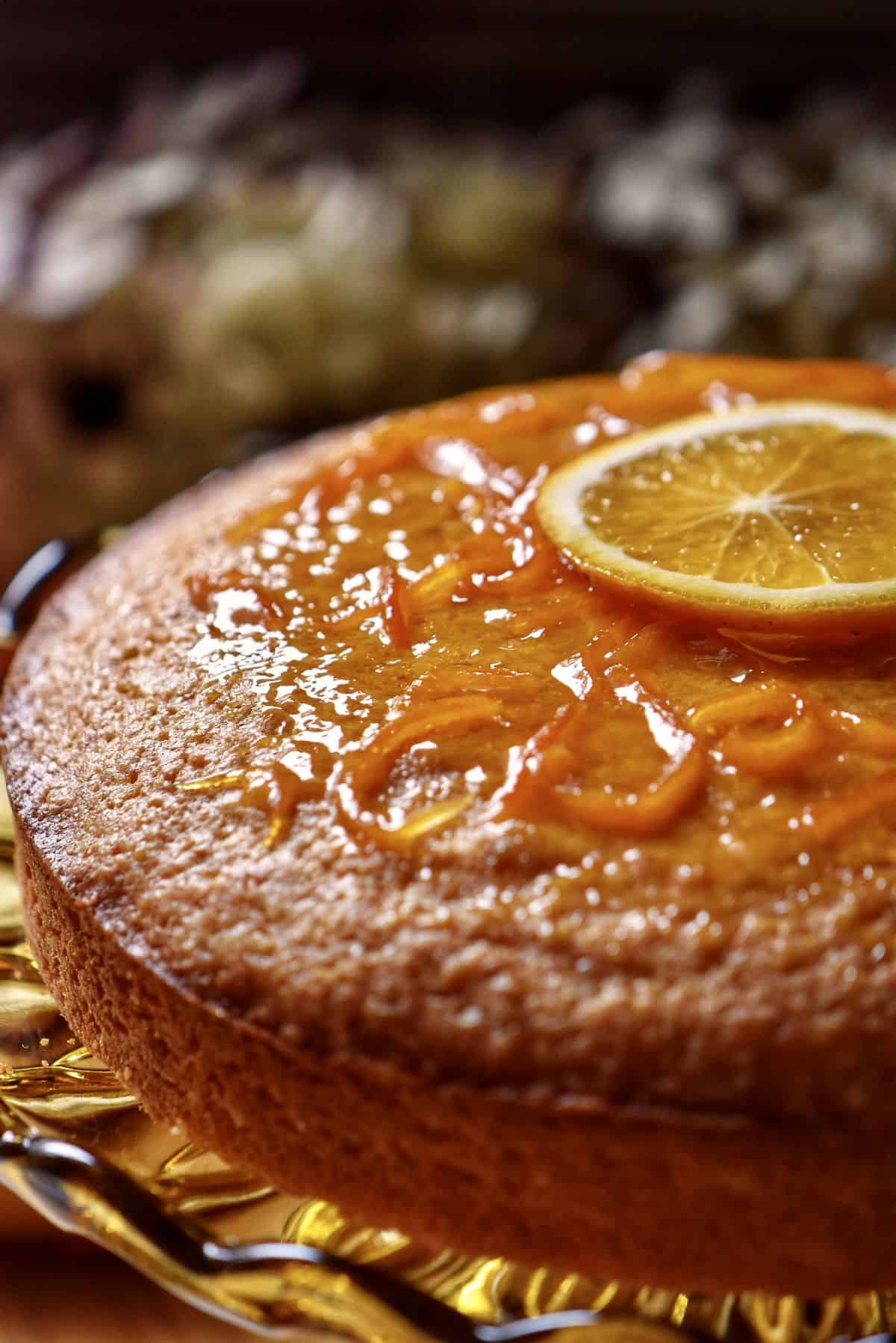 A glazed orange juice cake garnished with one slice of orange.