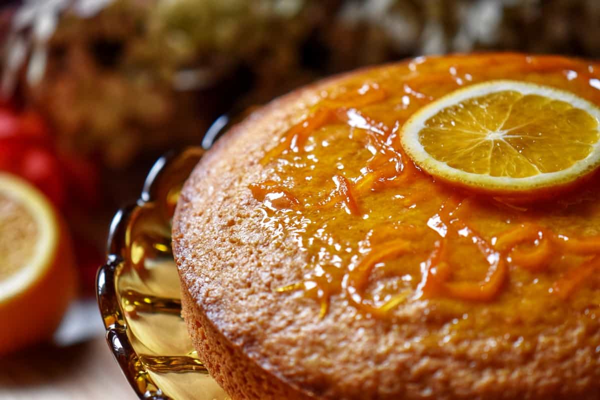 An orange glazed cake on a pedestal. 