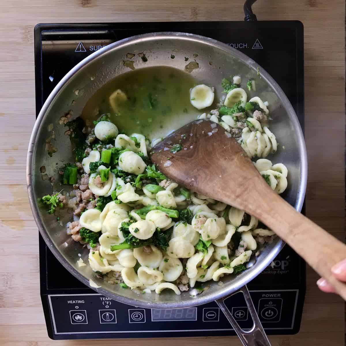 Pasta water in a saucepan of orecchiette, sausage and broccoli rabe.