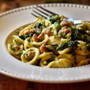 A white plate with orecchiette, Italian sausage and broccoli rabe.