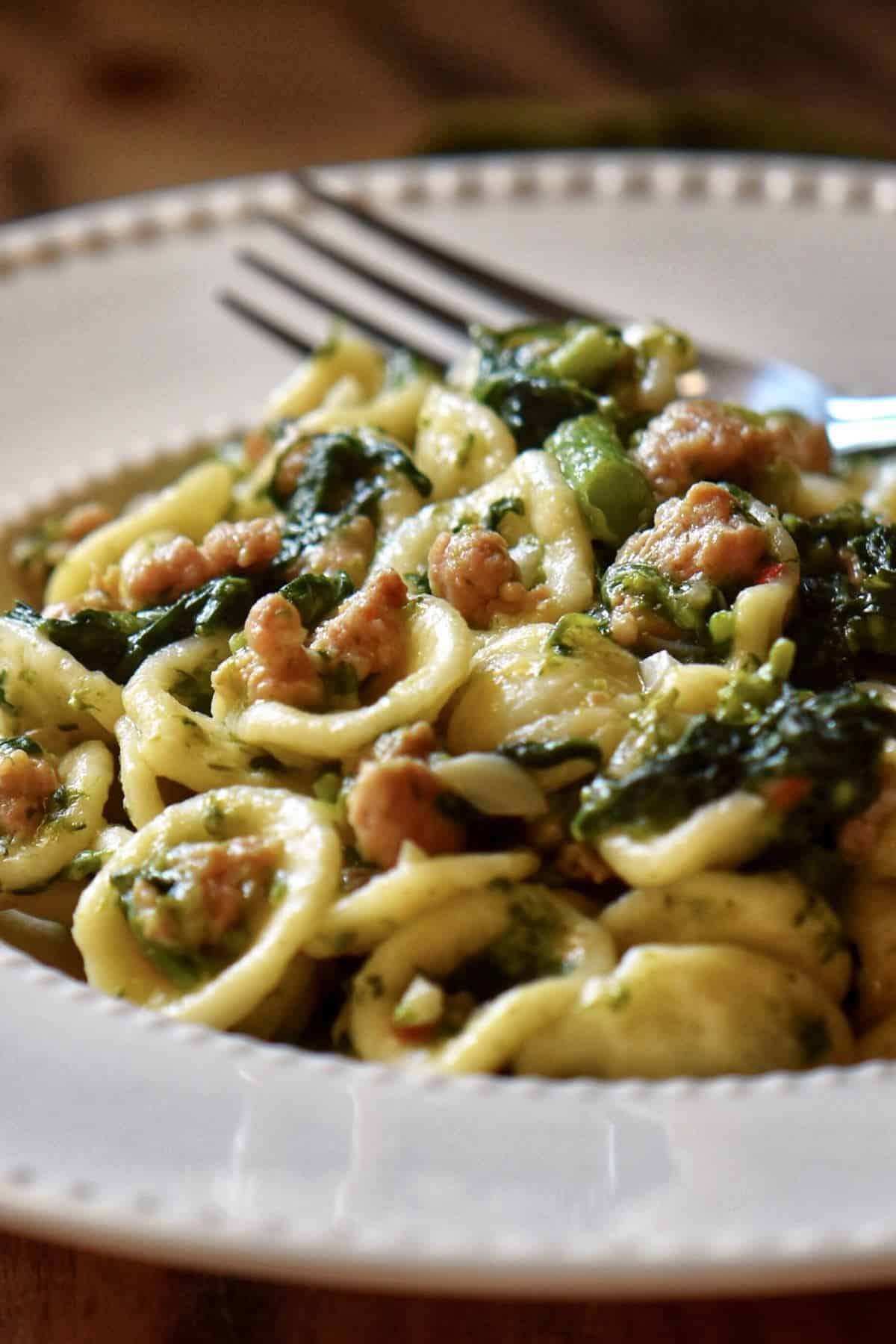 Pasta with rapini and Italian sausage in a white dish.