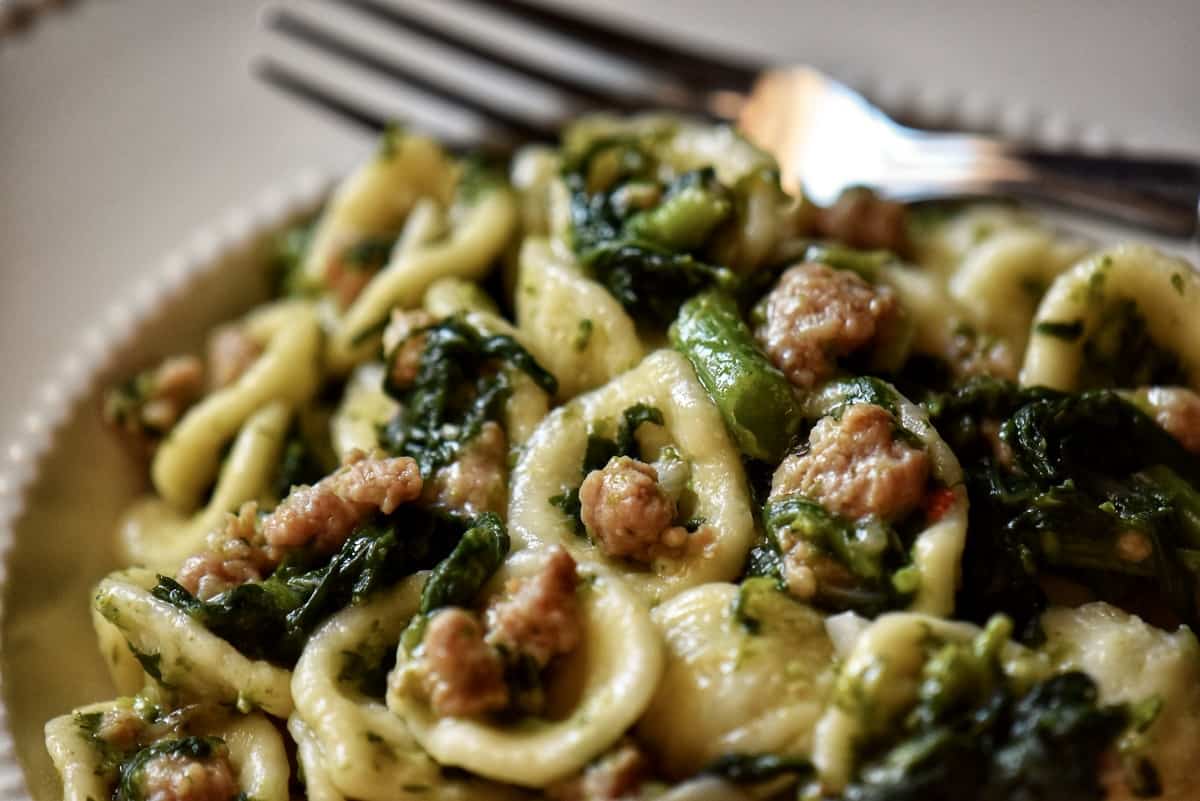 The combination of orecchiette pasta, broccoli rabe and Italian sausage in a white dinner plate.