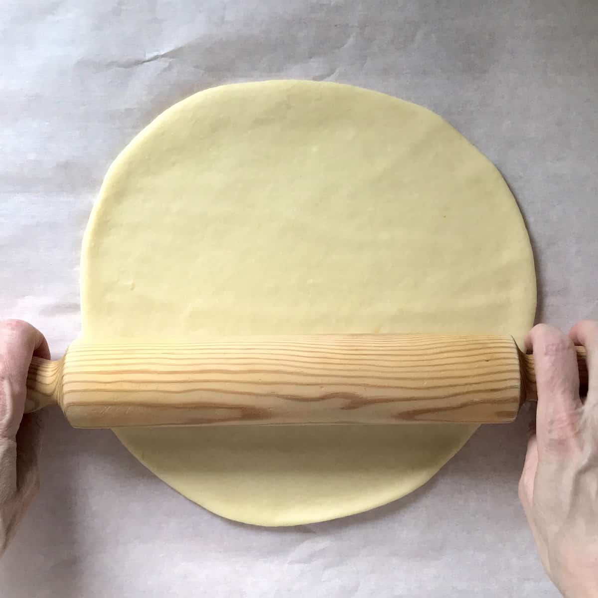 A ball of dough being rolled into a circle with a rolling pin.