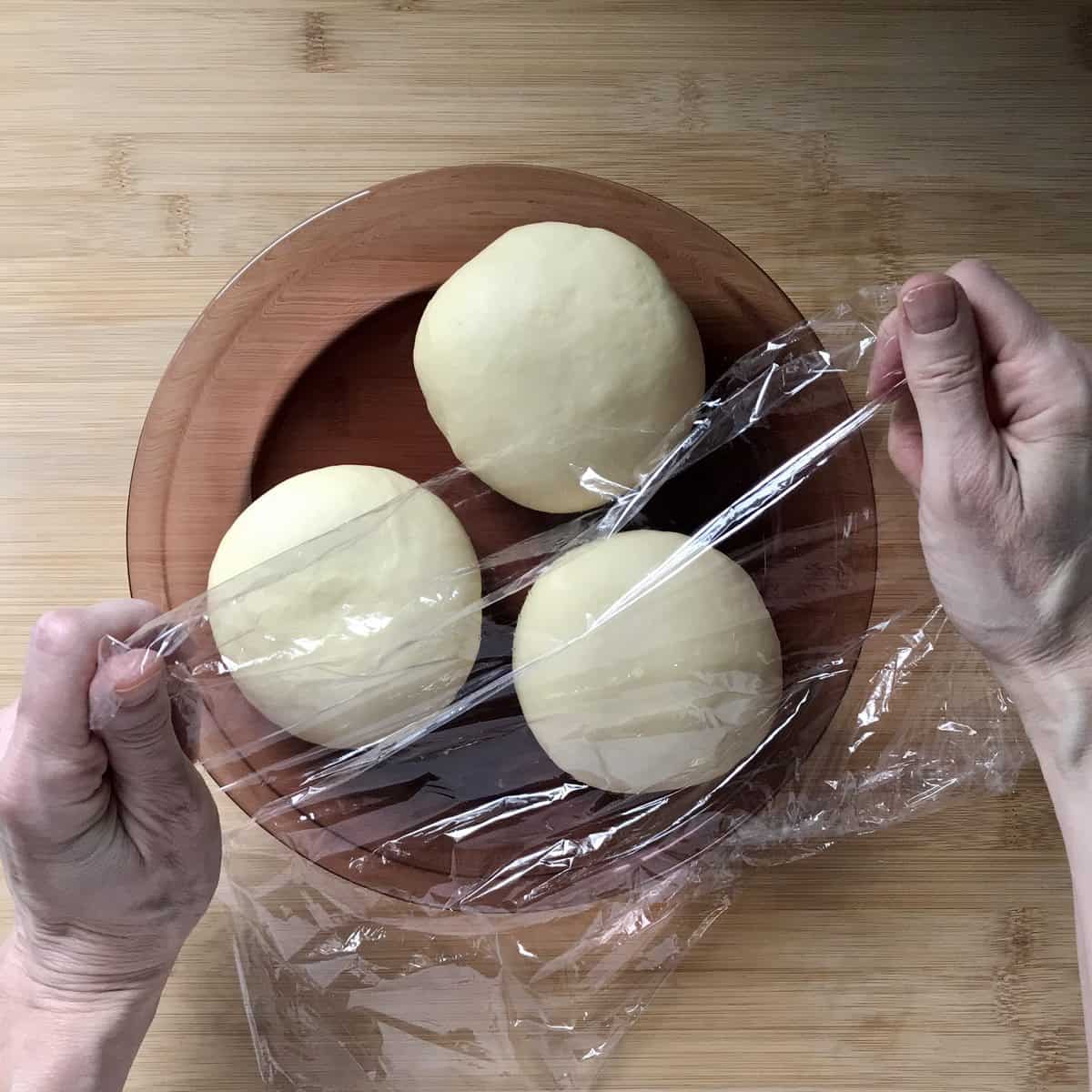 Three balls of dough being wrapped in plastic wrap. 