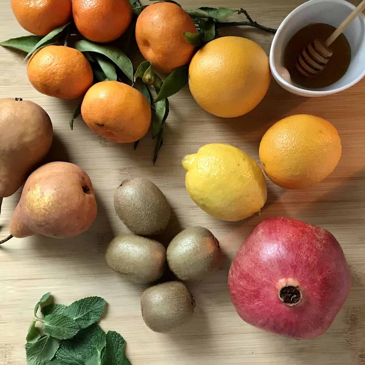 Fresh fruit, mint and a small bowl of honey on a wooden board. 