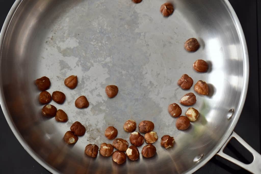 A handful of hazelnuts being roasted in a skillet.