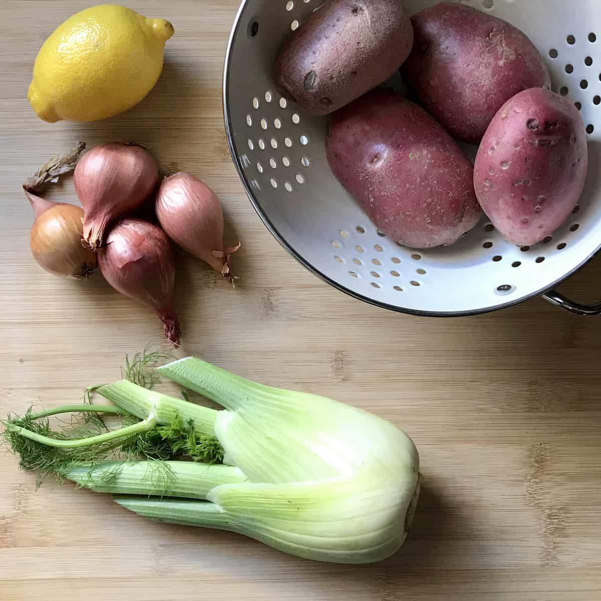 Fennel, red potatoes, lemon and shallots on a cutting board. 