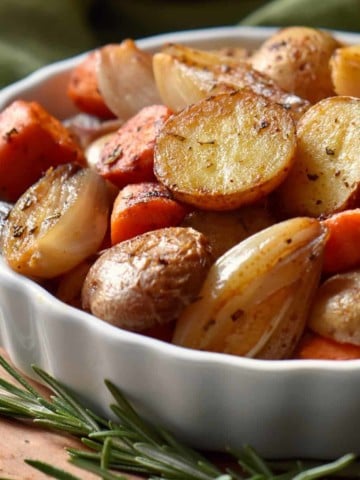 Oven roasted small potatoes and carrots in a white dish.