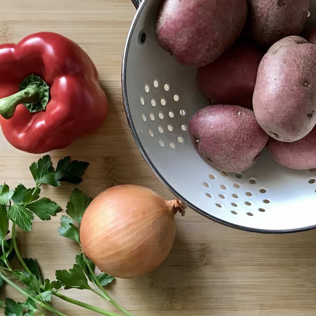 Red potatoes, a bell pepper, onions and parsley on a wooden board.