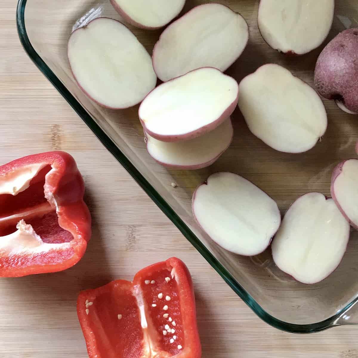 Halved potatoes and sliced red pepper on a cutting board.