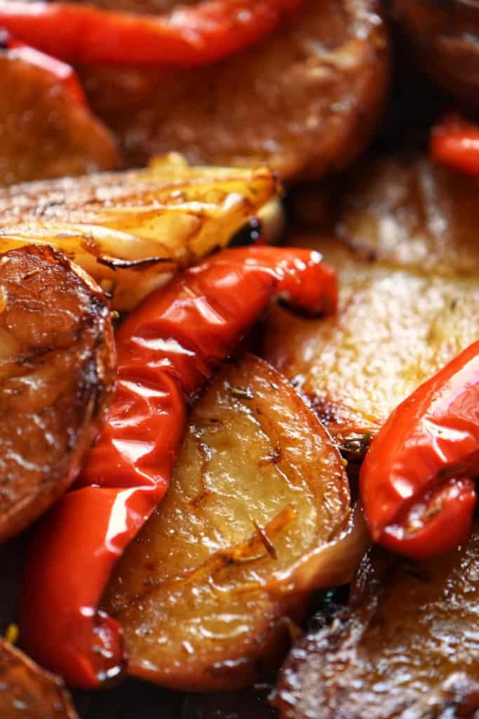 Roasted potatoes and red bell peppers in a baking dish.