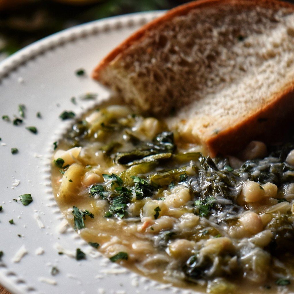 A close up phot of escarole white bean soup in a white soup bowl.