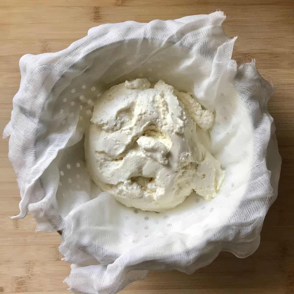 Ricotta cheese in a cheesecloth lined sieve. 