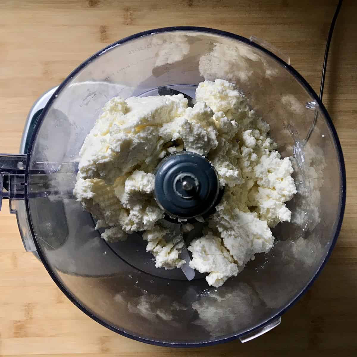 Fresh ricotta in teh bowl of a food processor. 