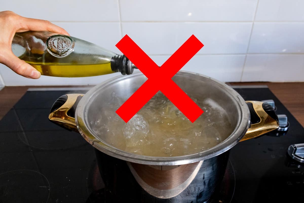 A red cross mark on olive oil being drizzled in a pot of pasta.