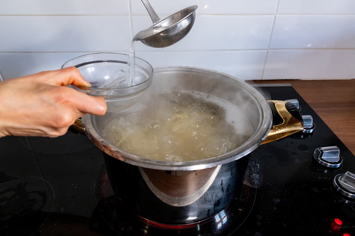 Starchy pasta water being removed from a pot of water.
