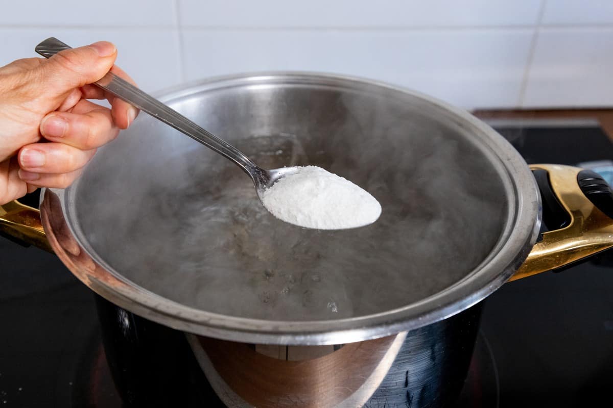 A tablepoon of salt being added to a pot of water. 