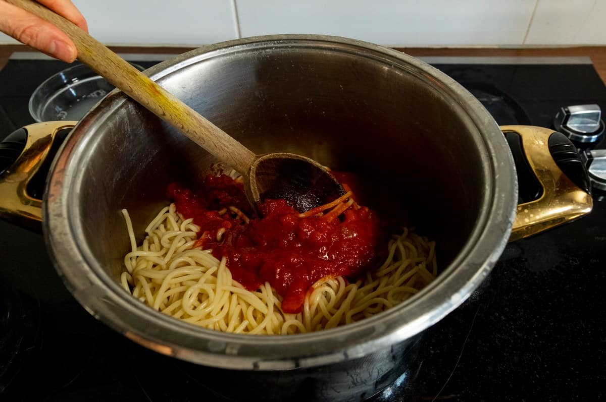 Pasta and sauce being combined in a pot.