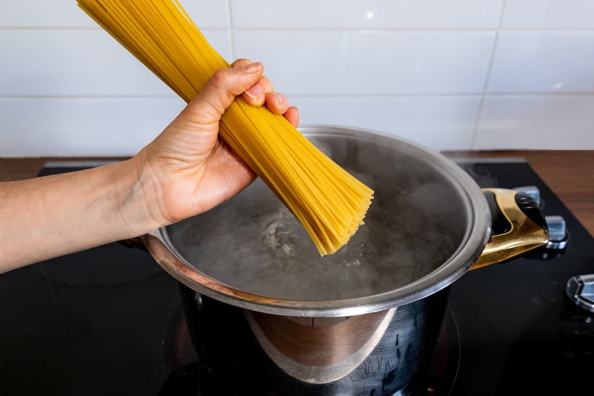 Spaghetti being dropped in a pot of boiling water.