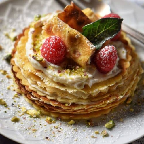 A mini crepe cake garnished with ricotta, raspberries and icing sugar.