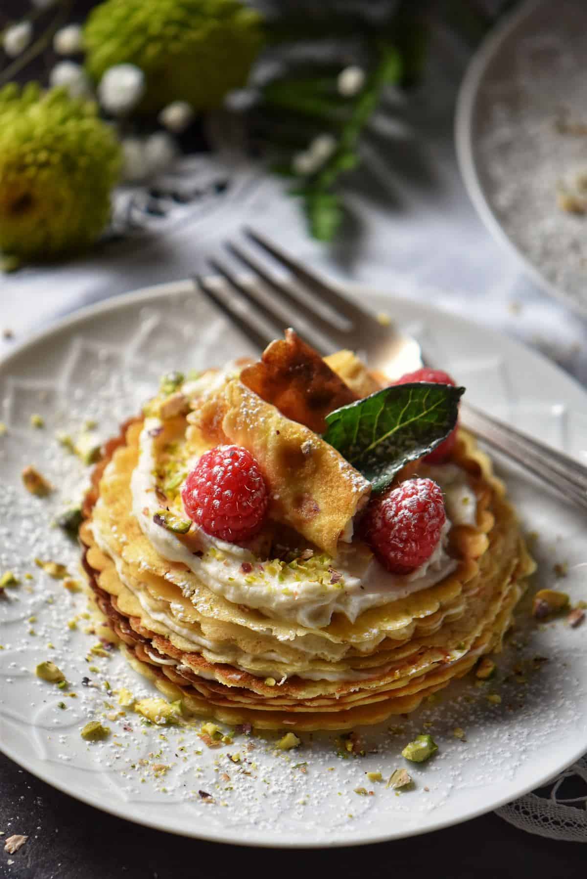 A mini crepe cake garnished with ricotta, raspberries and icing sugar.