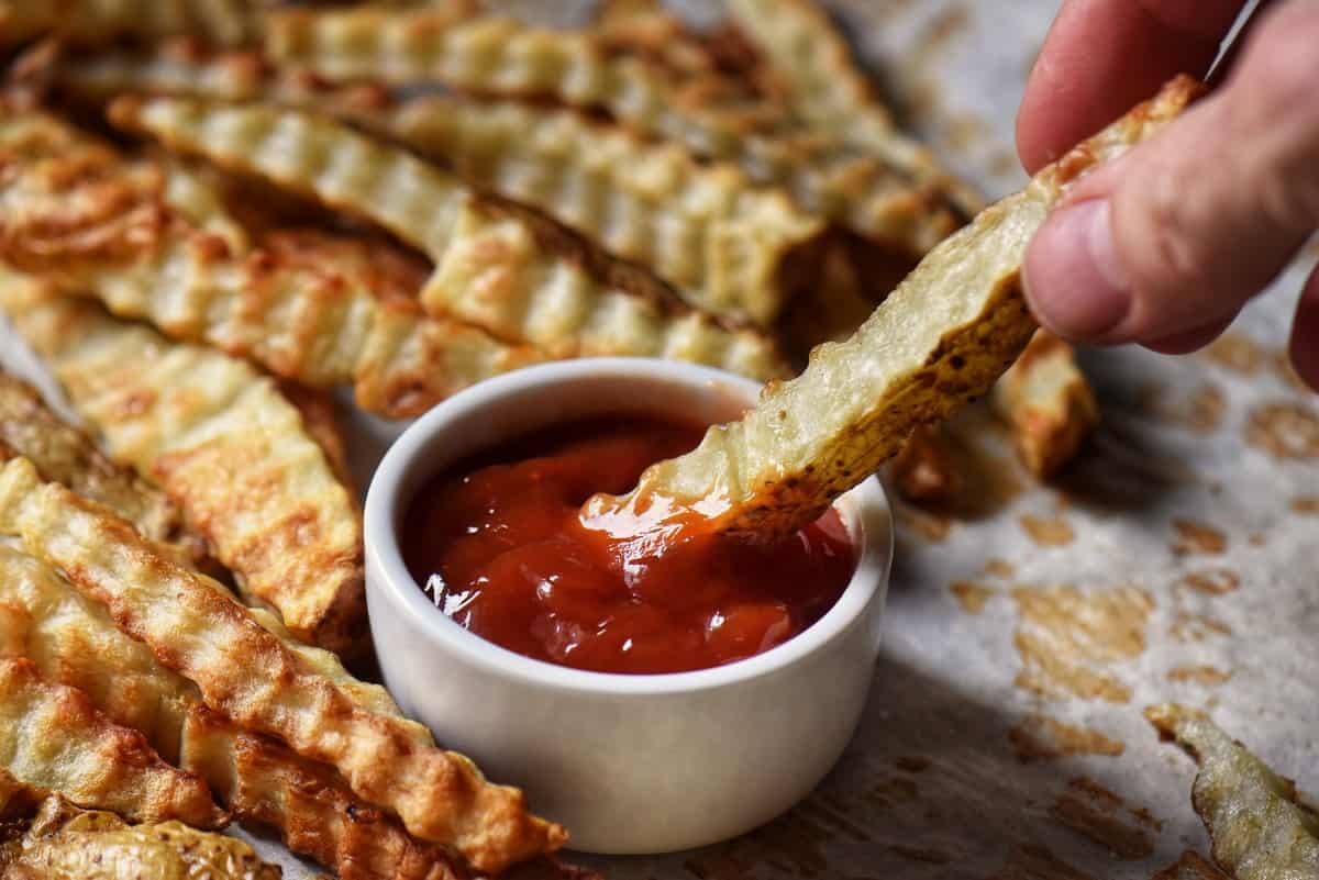 A wavy fry being dunked into a bowl of ketchup.