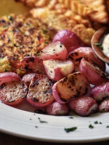 Roasted radishes next to tuna patties on a white plate.