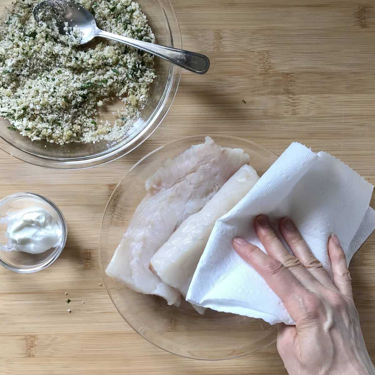 Cod fillets being patted dry with paper towels. 