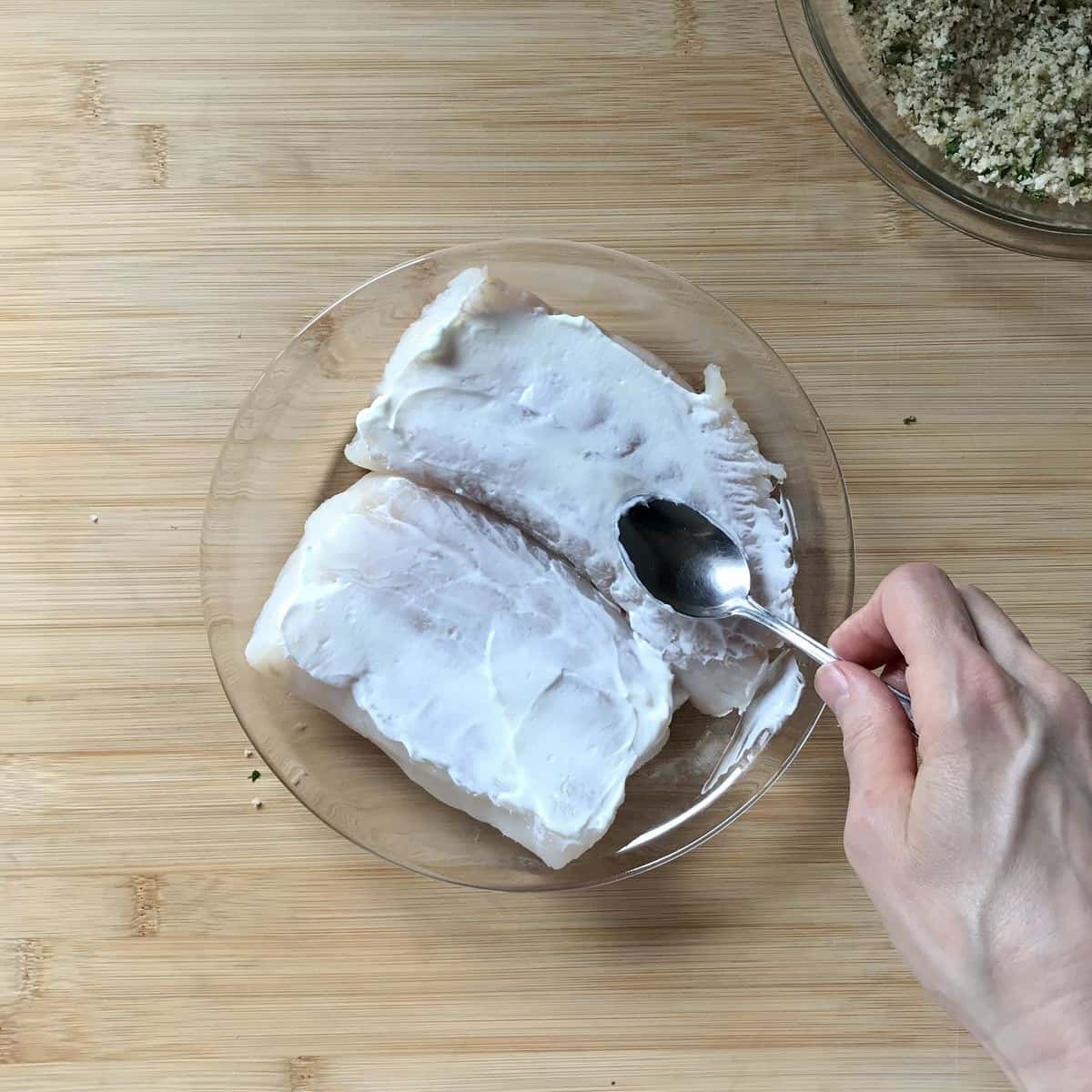 Greek yogurt being brushed on cod fillets. 