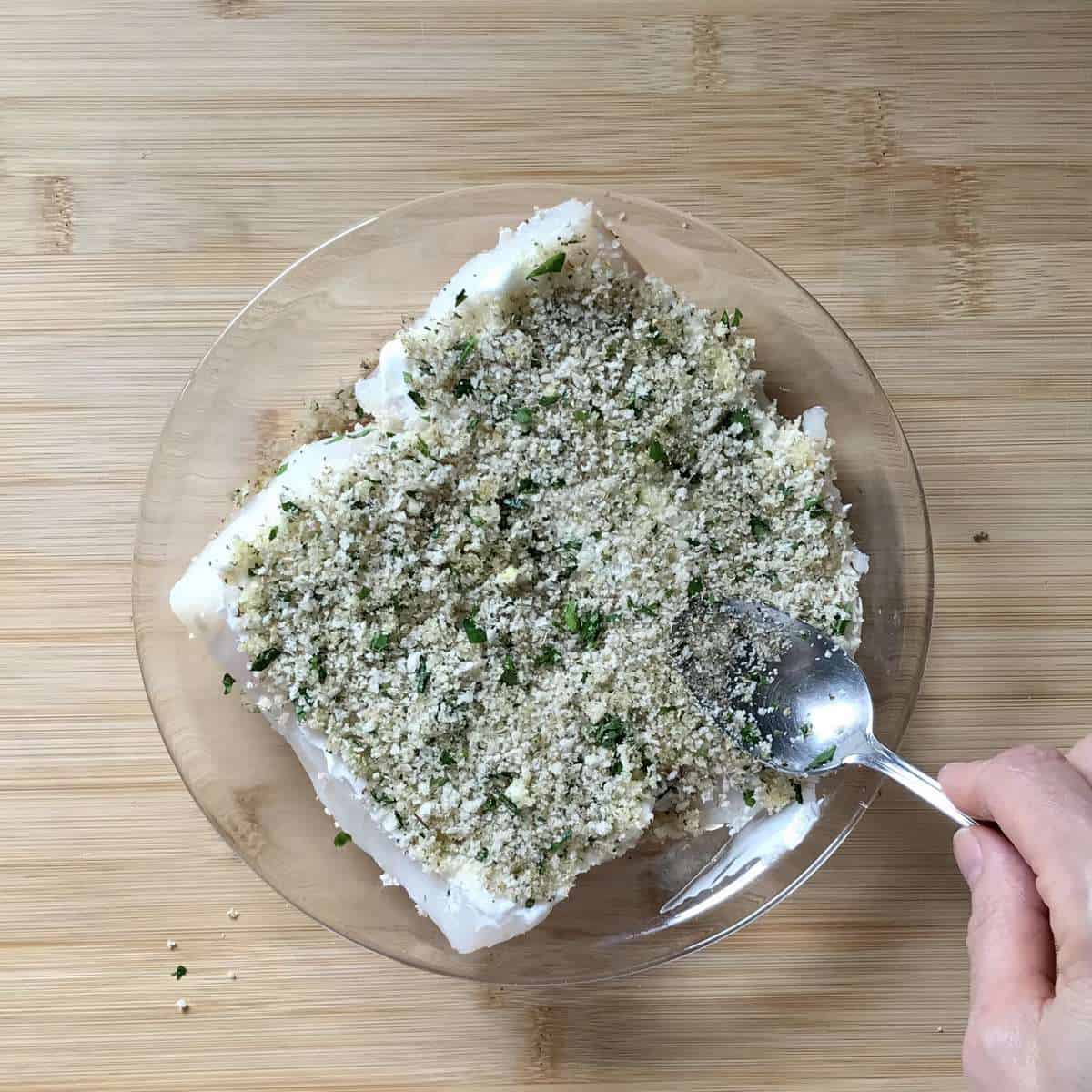 Panko topping being gently pressed on the tops of cod fillets. 