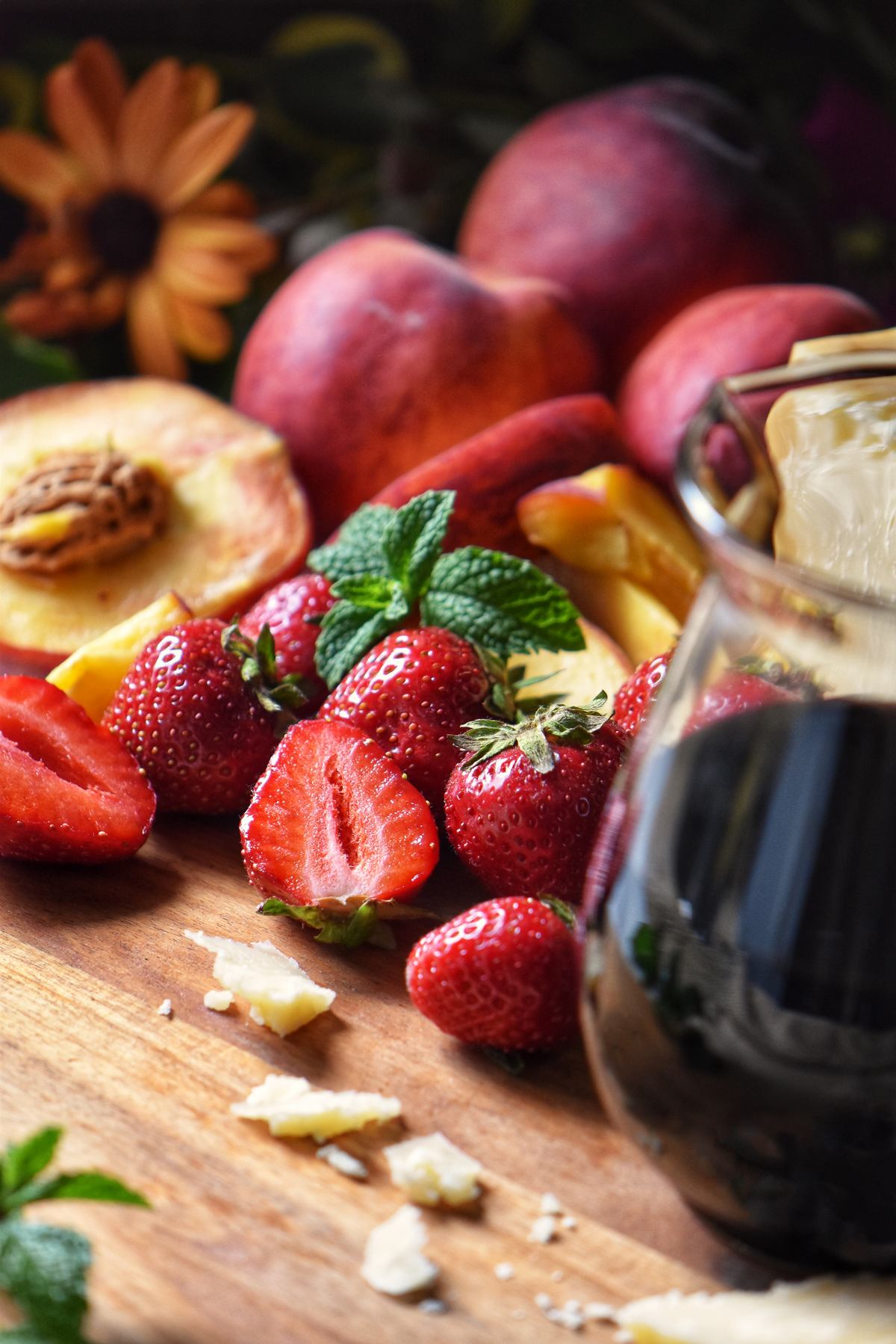 Balsamic glaze in a jar, next to fresh strawberries, peaches and cheese.