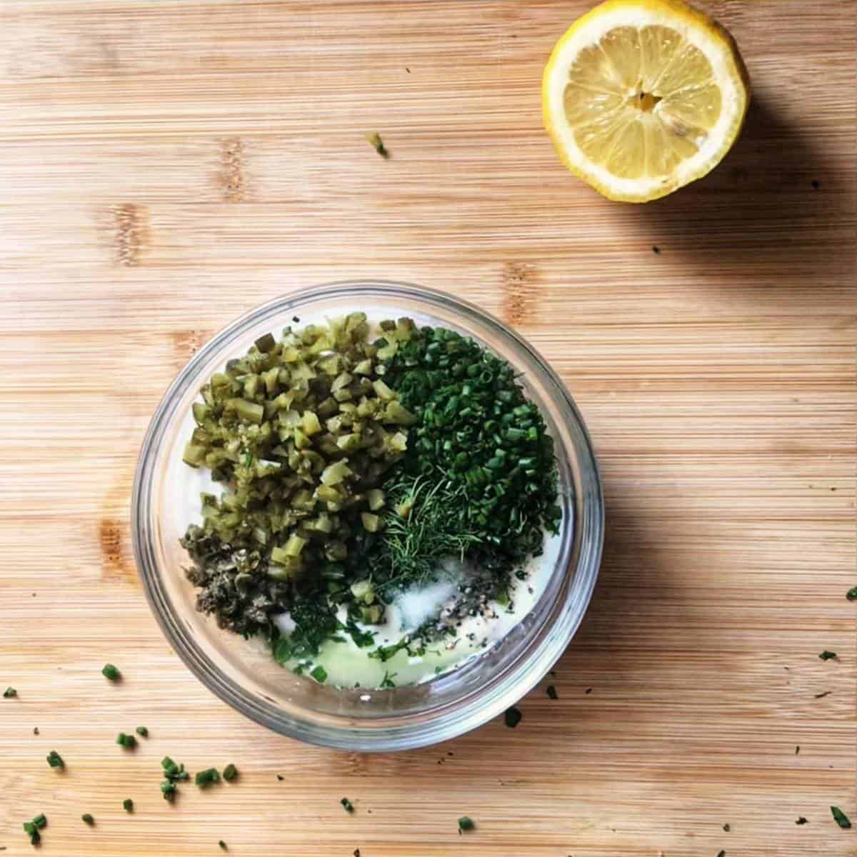 Ingredients for a no mayo tartar sauce in a bowl, next to half a lemon.