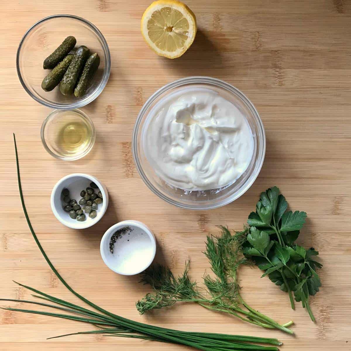 Ingredients to make tartar sauce on a wooden board.