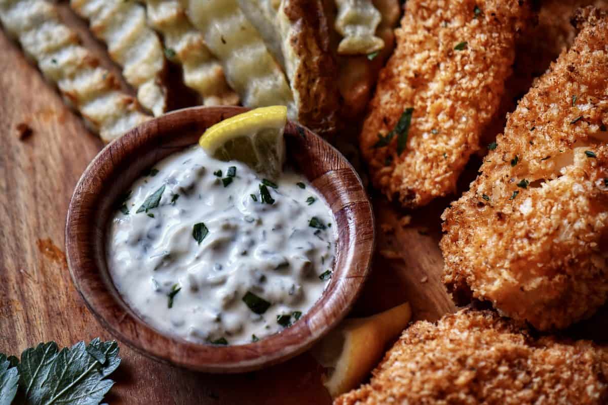 A close up of a no mayo sauce in a small bowl next to crinkle fries and fish.