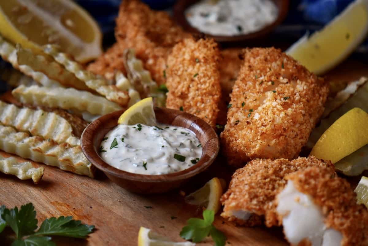 Tartar sauce surrounded by fish and chips.