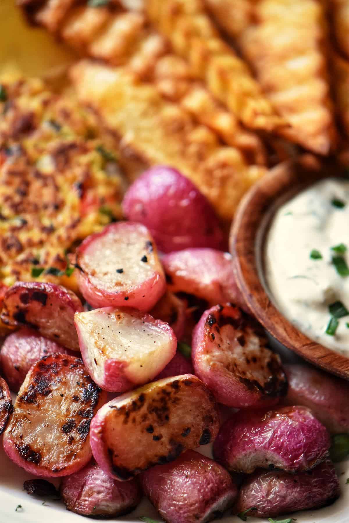 Roasted radishes next to tuna patties on a white plate.