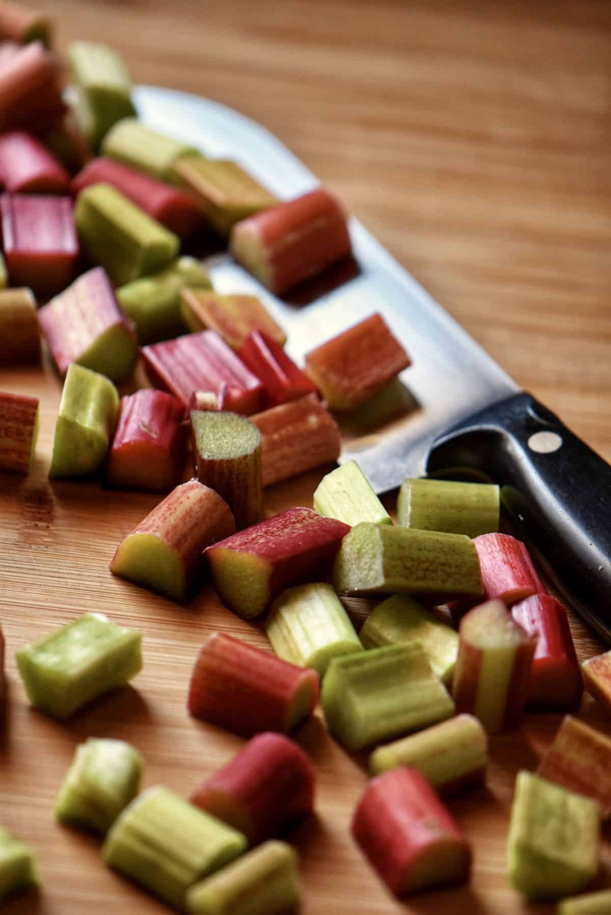 Diced rhubarb on a wooden board, next to a knife.