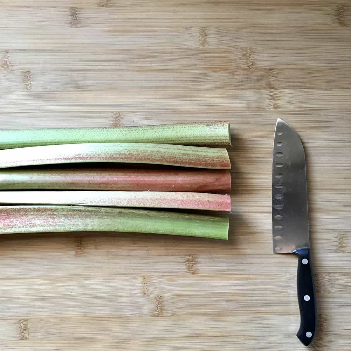 Rhubarb stalks next to a knife, lined up to get cut. 