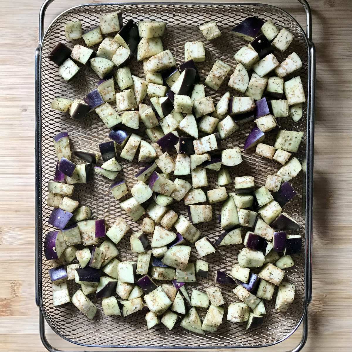 Diced eggplant spread on an air fryer basket.