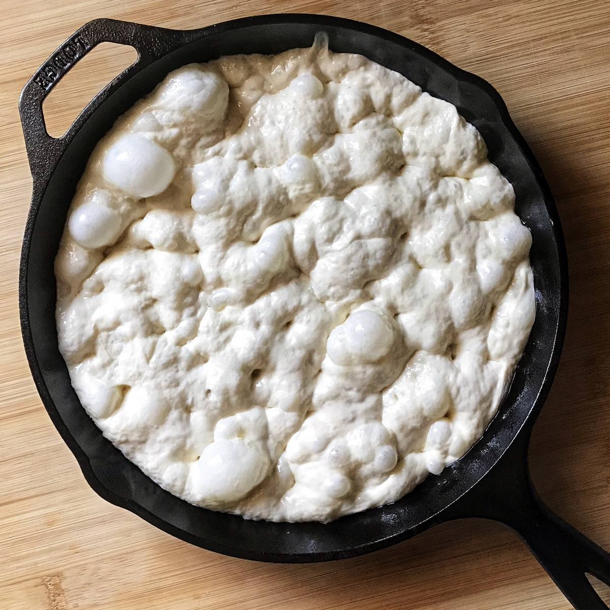 Dimpled focaccia dough in a cast iron pan.