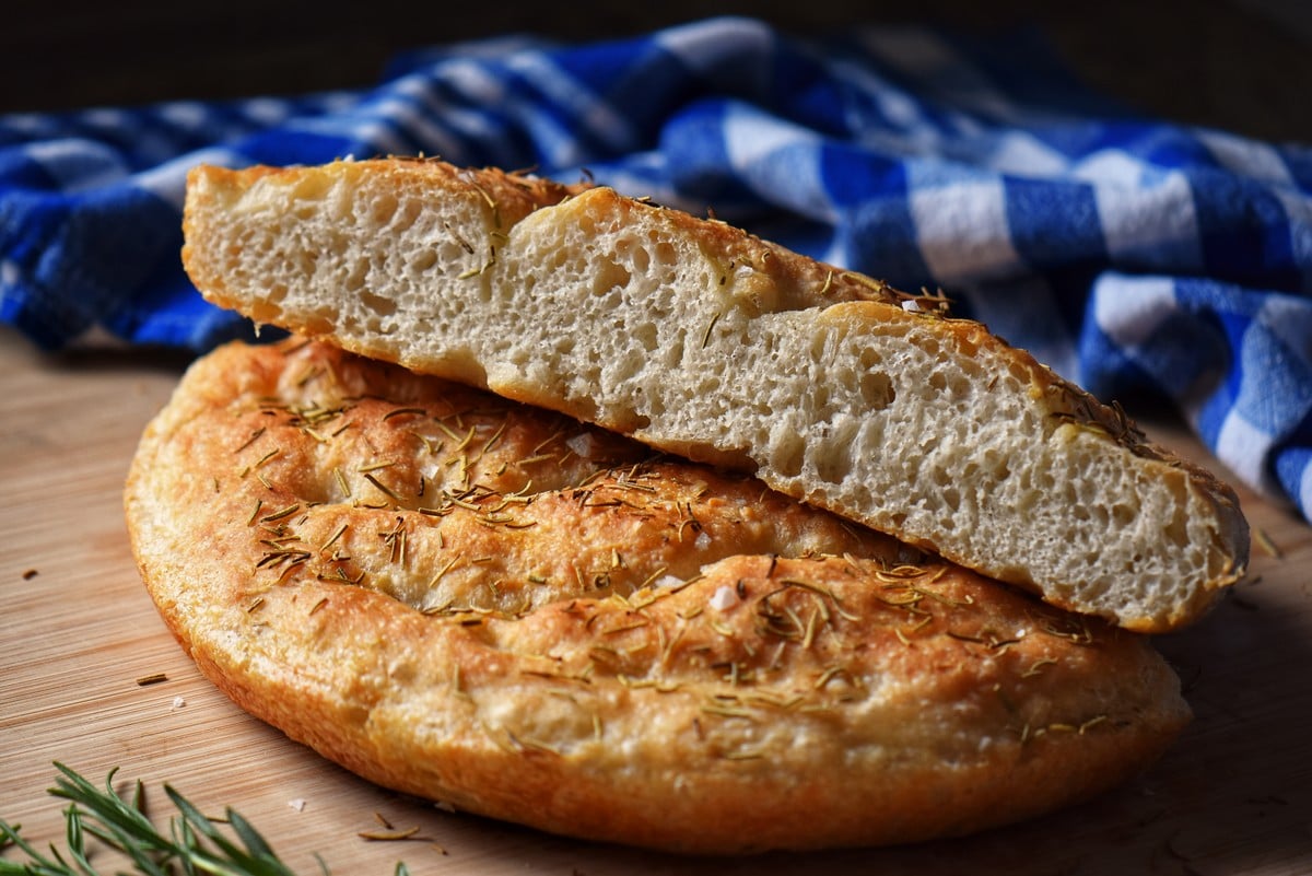 Rosemary focaccia dough cut in half on a wooden board.