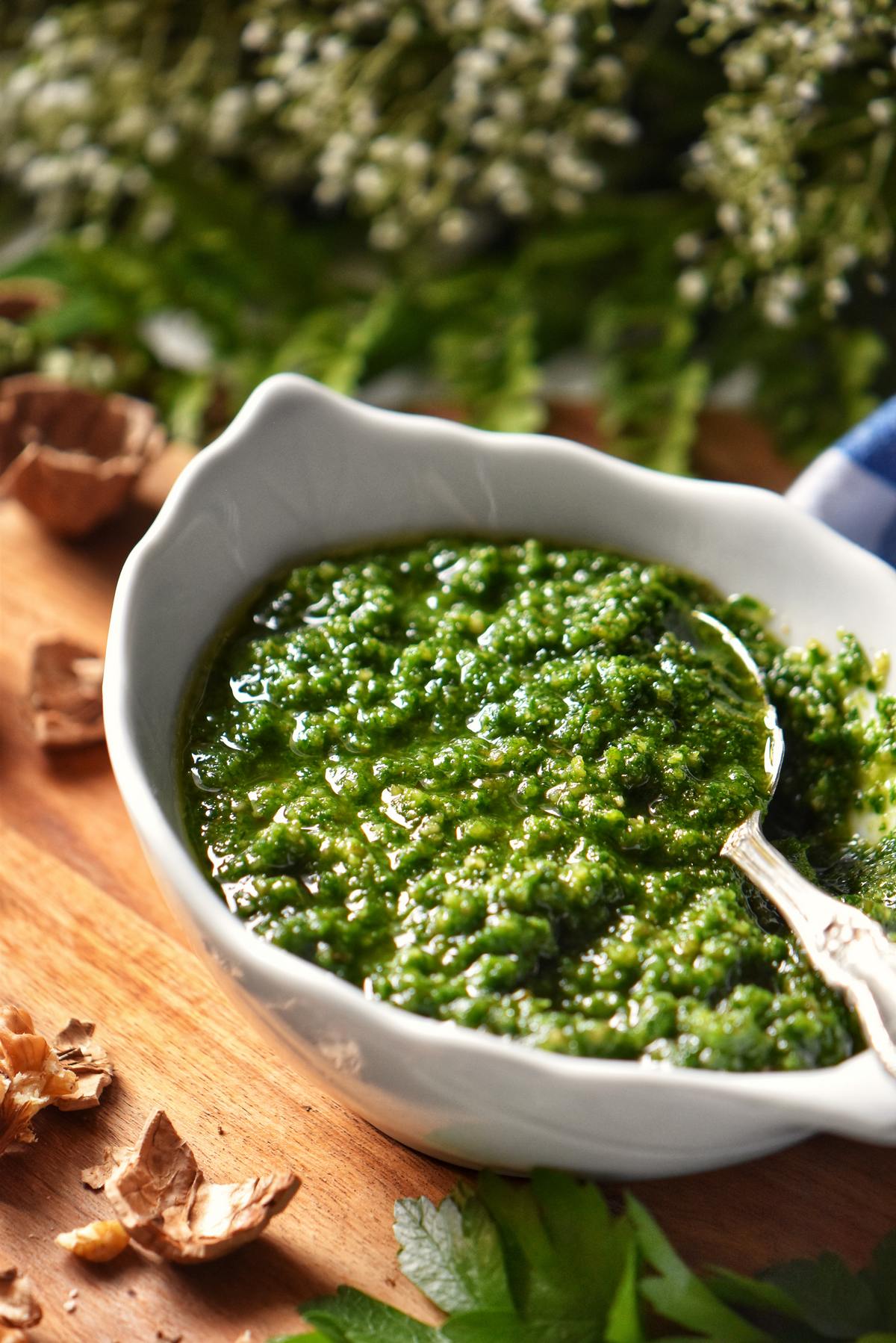 A spoon dipped into a white bowl of pesto made with parsley.