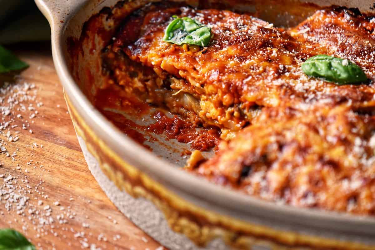 A casserole dish of eggplant parmesan with one portion missing.