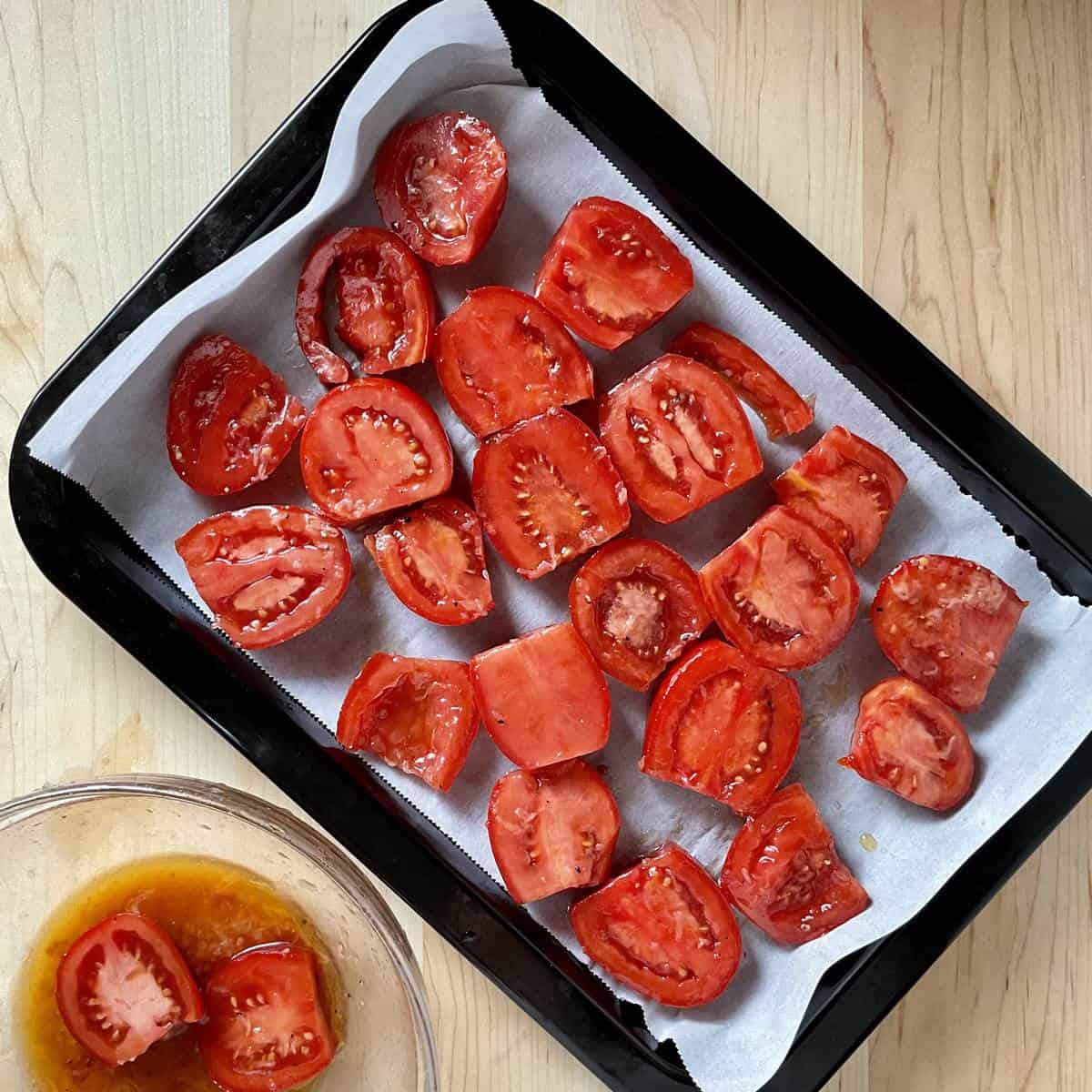Sliced tomatoes placed on a parchment lined roasting pan.