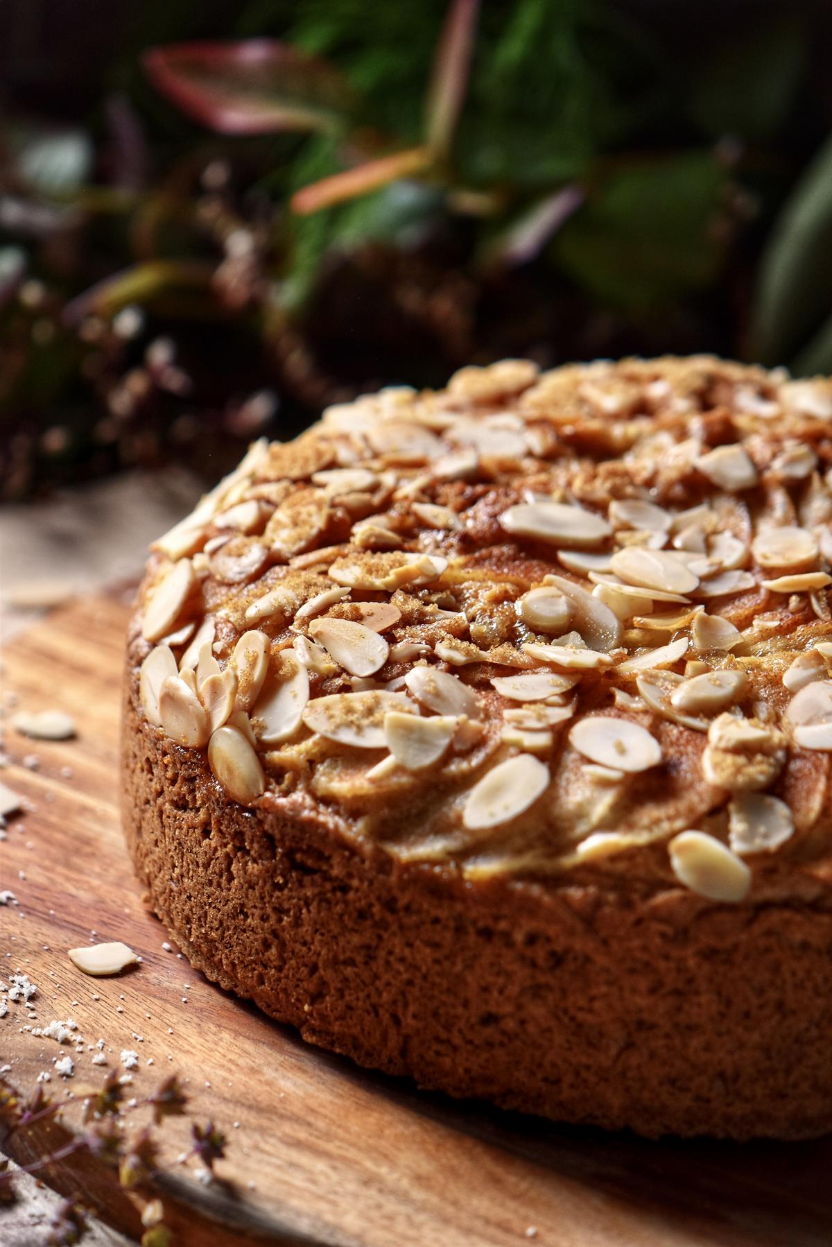 A pear cake garnished with sliced almonds on a wooden board.