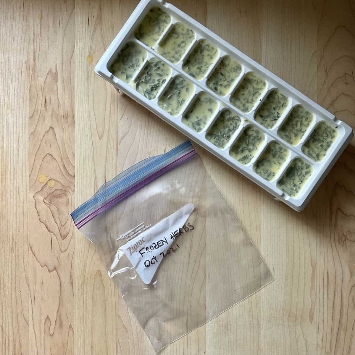 An ice cube tray of herbs next to a Ziploc bag.